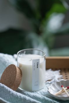 a glass candle sitting on top of a table next to a white plate with matches