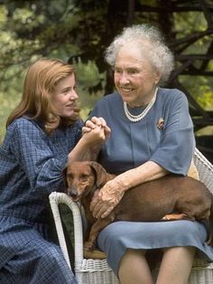 an older woman sitting next to a younger woman holding a dog on a wicker chair