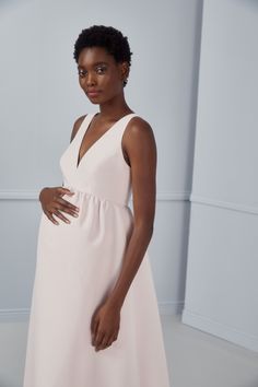 a pregnant woman in a white dress poses for the camera with her hands on her belly