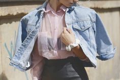 a woman wearing a denim jacket and pink shirt is holding her hand in her pocket