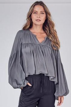 This is the absolute perfect blend of elegance, sexiness and class in one gorgeous, lightweight blouse. It’s loose fitting and flowy but balanced out with a shorter front hem. It’s not a crop, but could show a peak if you really wanted to. With balloon sleeves, a hooked closed neckline and silky feel, you will be the showstopper in any room you enter. Colors: Ash Olive and Orchid Mist Balloon Sleeves Hook Neck Closure Loose Fitting Subtle Mid-back Ruffle 100% Polyester Suggested Care: Hand Wash Flowy Blouse Outfit, Boho 2024, Boho Long Sleeve Shirt, Swift Outfits, Contemporary Loft, Flowy Shirt, Balloon Sleeve Top, Feminine Top, Taylor Swift Outfits