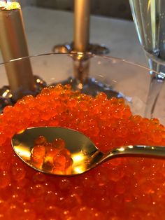 the spoon is full of orange jelly and sits on the table next to two champagne glasses