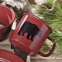 two red mugs sitting next to each other on top of a wooden table with pine branches