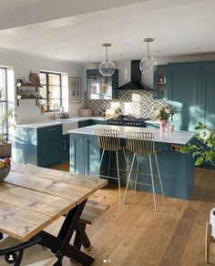 a kitchen with wooden floors and blue cabinets, an island table and stools in the center