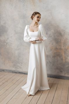 a woman in a long white dress standing on a wooden floor with her arms crossed