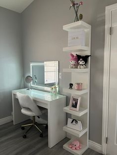 a white desk topped with a computer monitor next to a mirror and shelf filled with stuffed animals