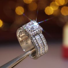 a diamond ring is being held up by a tweep with some lights in the background