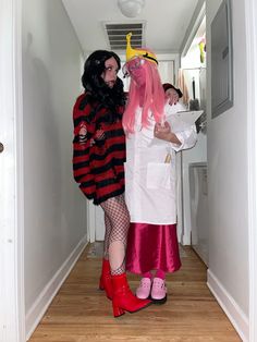 two women dressed in costumes standing next to each other on a wooden floored hallway