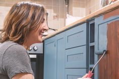 a woman is smiling while painting the kitchen cabinets with blue paint and a pair of scissors