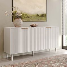 a white sideboard sitting on top of a wooden floor next to a vase filled with flowers