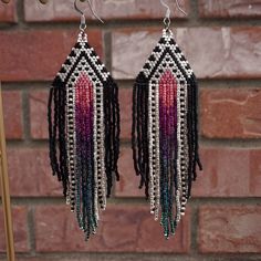 two pairs of beaded earrings with fringes hanging from hooks against a brick wall