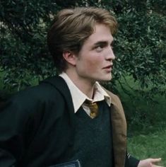 a young man dressed in harry potter clothes and holding a book while standing next to a tree