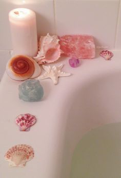 various seashells and candles sit on the edge of a bathtub