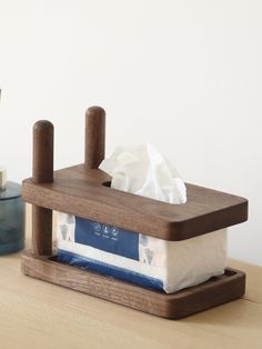 a tissue dispenser sitting on top of a wooden table next to a blue vase