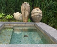 two vases sitting next to each other on top of a pool in a garden