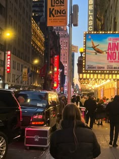 people are walking down the street in new york city at night with large billboards