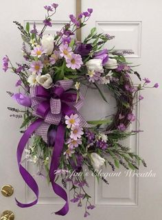 a wreath with purple and white flowers hanging on a door