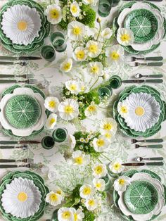 the table is set with green and white plates, silverware, and flower centerpieces