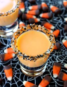 two glasses filled with orange and black candy sitting on top of a table covered in halloween candies