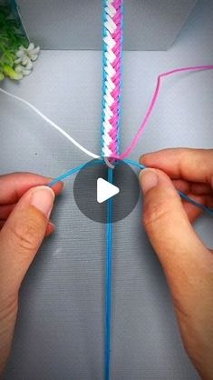 two hands are working on an object with blue and pink yarn, while another hand is holding the string