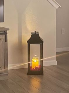 a lit candle sitting on top of a wooden floor next to a tv mounted on a wall