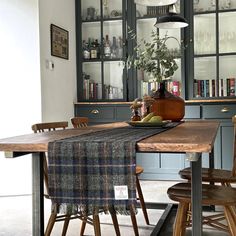 a dining room table with chairs and a plaid table cloth on it, in front of some bookshelves