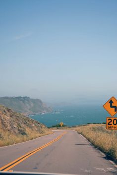 a road sign on the side of an empty road with mountains in the background and blue sky