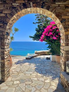 an arch leading to the ocean with pink flowers on it and blue water in the background