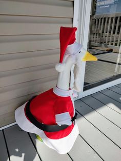 a stuffed duck wearing a santa claus outfit on the front porch with its head sticking out