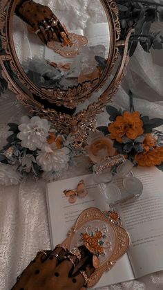 an open book on a table next to a mirror with flowers and other items around it