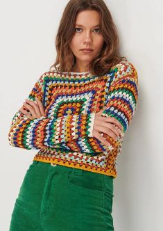 a woman wearing green pants and a multicolored sweater poses with her arms crossed