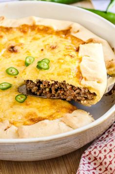 a close up of a pie in a pan on a wooden table with green peppers