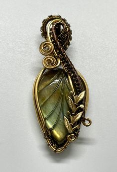 This stunning pendant features a beautifully carved Labradorite leaf, its iridescent flashes of color complemented by the warm tones of intricately wire-wrapped brass. Brass leaves accent the design, adding a touch of nature-inspired elegance. The unique glow of the Labradorite, paired with the rich, earthy brass, makes this pendant a captivating statement piece perfect for any occasion. A celebration of natural beauty and artisanal craftsmanship, it’s an eye-catching addition to any jewelry col Gold Freeform Wire-wrapped Jewelry, Gold Wire Wrapped Freeform Jewelry, Gold Freeform Wire Wrapped Jewelry, Unique Gold Labradorite Jewelry, Bohemian Brass Leaf Jewelry, Artisan Freeform Gold Jewelry, Bohemian Leaf-shaped Brass Jewelry, Bronze Hand Wrapped Pendant Jewelry, Hand Wrapped Bronze Pendant Jewelry