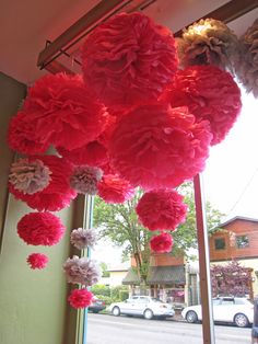 red and pink tissue pom poms hanging from the ceiling in front of a window