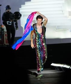 the man is walking on stage with his arms in the air while wearing a colorful outfit