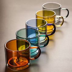 five different colored glass mugs lined up in a row on a gray table top