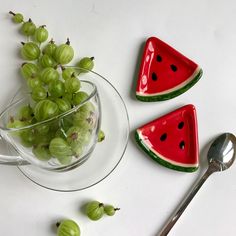 some grapes and watermelon slices are in a glass bowl next to a spoon