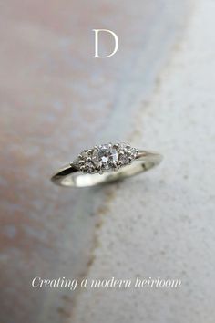 a three stone diamond ring sitting on top of a white surface with the letter d above it