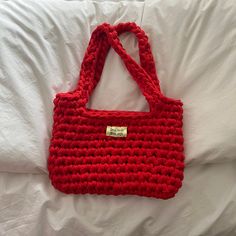 a red crocheted bag sitting on top of a white bed next to pillows