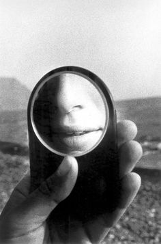 a person looking through a magnifying glass at the camera with mountains in the background