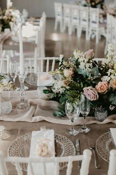 the table is set with white and pink flowers, silverware, candles and napkins