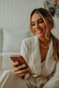 a woman sitting on the floor looking at her cell phone while smiling and holding it