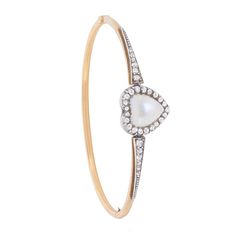 Dating back to the 1880s, this bangle centres a heart shaped, cabochon cut Moonstone. It has been rub over set and haloed by rose cut diamonds. The diamonds continue down the shoulders and have a total weight of 0.30 carat. The stones are set with silver, typical of era, and the bangle is made in 15 carat rose gold. The bangle is fitted with a a safety chain and a secure clasp. Gemstone: Moonstone Stone Shape: Cabochon, Heart Metal: 15ct Rose Gold, Silver Age: 1880s