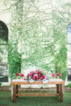 a wooden table with flowers on it in front of a wall covered in vines and ivys