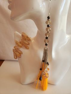 Orange tassel, silver chain earring dangles; orange semi-precious stone bracelet; orange oval bead ring silver dots trim Earrings Orange Tassels 5.51" / 14 cm (Polyester Mala Tassel) Metal Silver Total Length: 5.51" / 14 cm; Tassel Length: 5.12" / 13cm Thickness / Cap Size: 1cm Material: Polyester Earring length 9" with beige and black acrylic beads cascading down to tassel  Bracelet is biege/cream semi-precious stones. 8 inches wide Ring, stretch, gold-finished "pewter" (zinc-based alloy), 21mm wide with 25x18mm non-calibrated oval setting, size with a Cabochon setting: cat's eye glass, orange, 25x18mm calibrated oval, quality grade. Elegant Metal Jewelry With Tassels, Elegant Metal Tassel Jewelry, Amber Dangle Jewelry With Matching Earrings, Elegant Bracelet With Dangling Beads For Gift, Amber Beaded Jewelry For Party, Amber Spiritual Dangle Jewelry, Elegant Yellow Long Drop Jewelry, Adjustable Bracelet With Dangling Beads, Bohemian Drop Earrings With Adjustable Chain