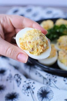 a person holding an egg in their hand with other food on the plate behind them