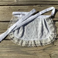 a white dress with lace on it sitting on top of a wooden table next to a piece of cloth