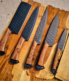 five knives lined up on top of each other next to a piece of butcher block