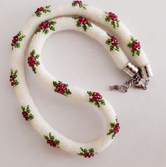 a white beaded dog leash with red and green flowers on it's side