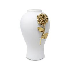 a white vase with a gold flower on the front and bottom, sitting on a white surface